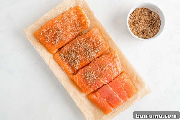 Seasoned salmon fillets, coated in a homemade BBQ rub. Four fresh salmon fillets neatly arranged on a plate, generously seasoned with a rich, dark dry rub, ready for cooking.