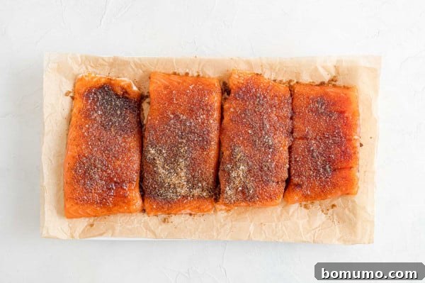 Ready-to-cook BBQ salmon fillets, perfectly seasoned and awaiting the skillet. Four seasoned BBQ salmon fillets resting on a parchment-lined plate, allowing the dry rub flavors to meld before cooking.