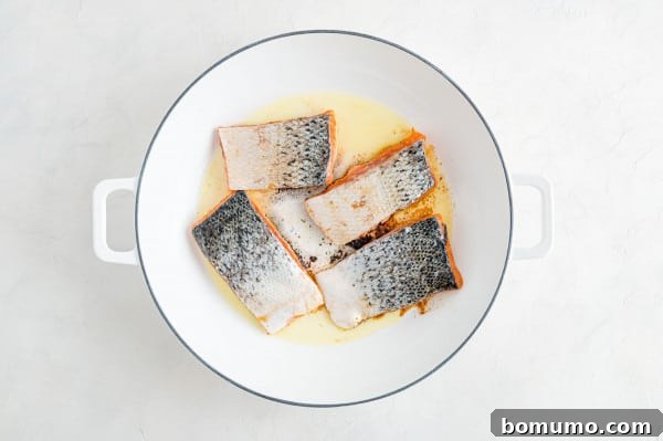 Searing BBQ salmon skin-side up for a perfectly caramelized crust. Salmon fillets being seared skin-side up in a hot cast iron skillet, creating a beautiful crust on the top surface.