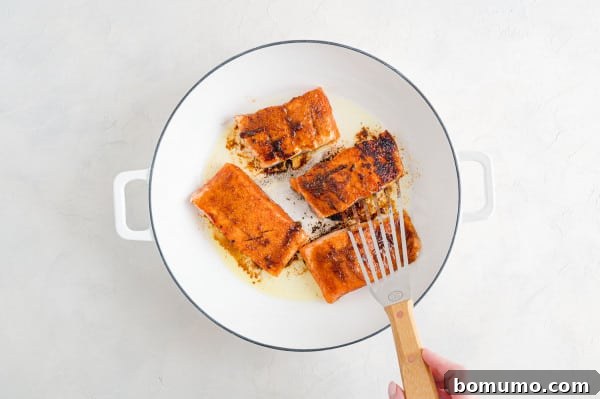 Crispy skin in progress: salmon fillets searing skin-side down. Flipped salmon fillets, now searing skin-side down in the hot skillet, ensuring crispy skin development.