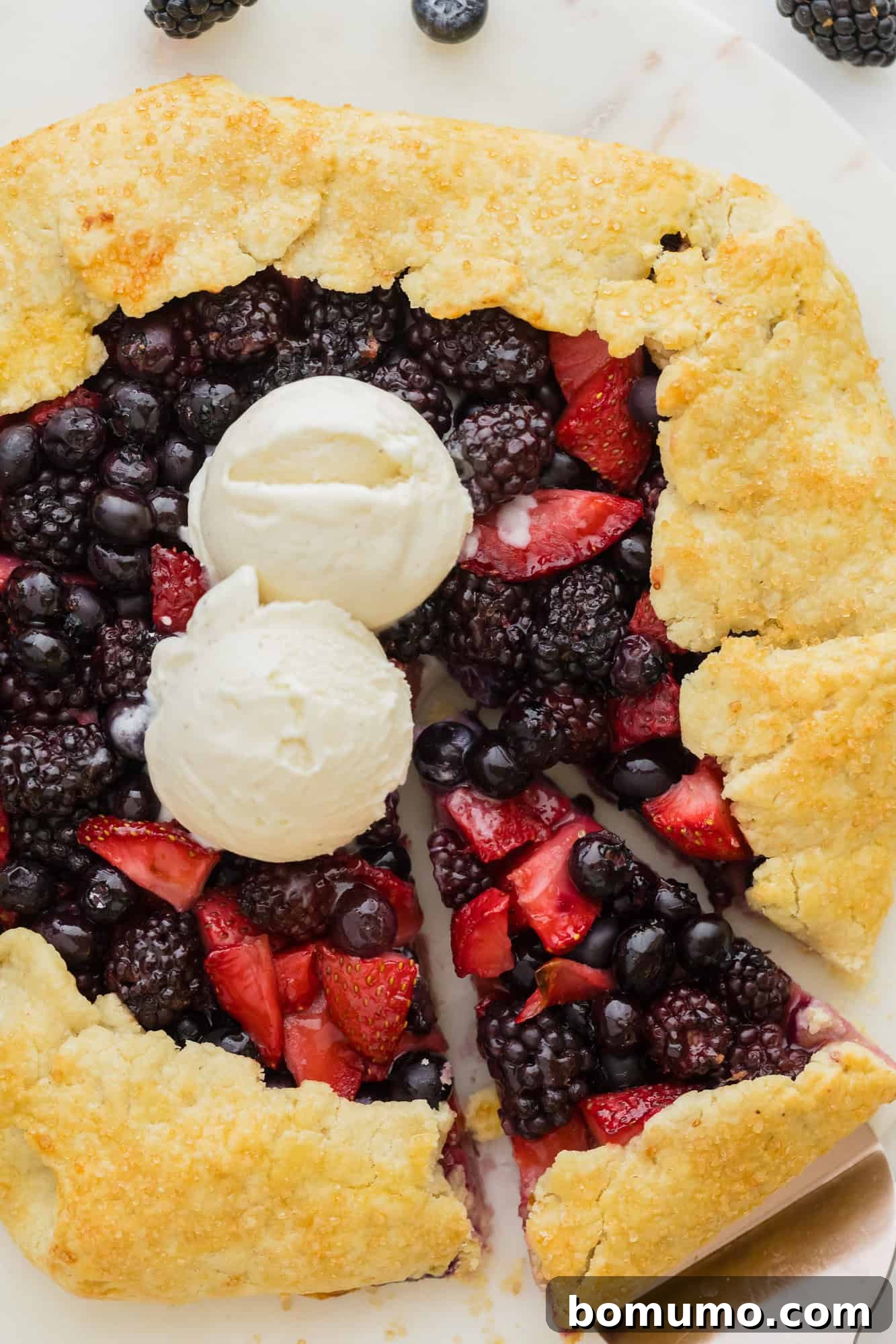 A stunning berry galette, beautifully golden, with a slice already cut and two scoops of creamy vanilla ice cream melting on top.