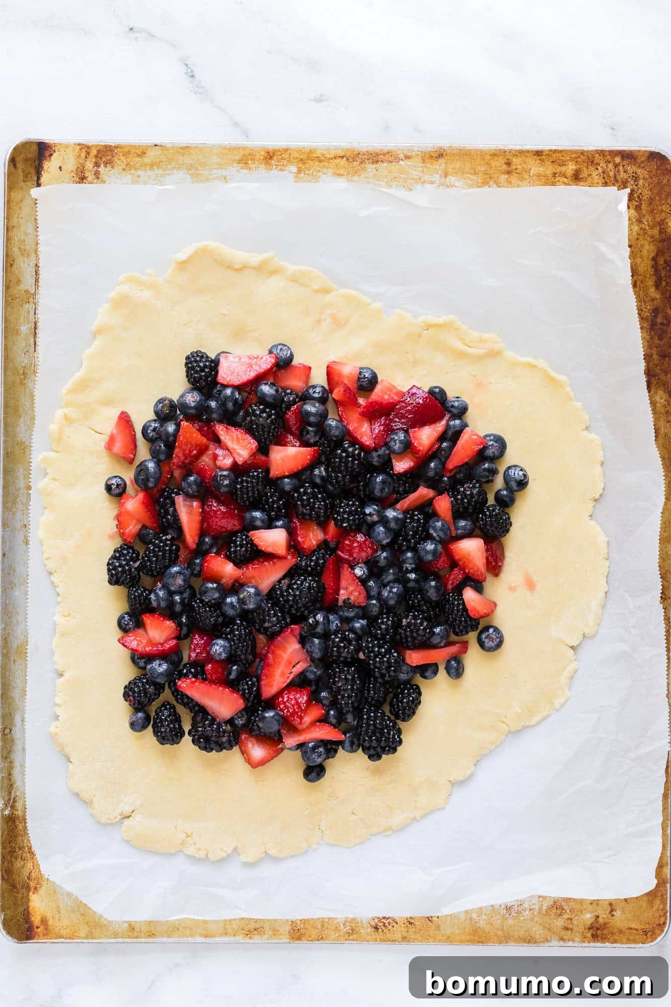 Fresh berries are artfully arranged on the pie crust, with the border still unfurled.