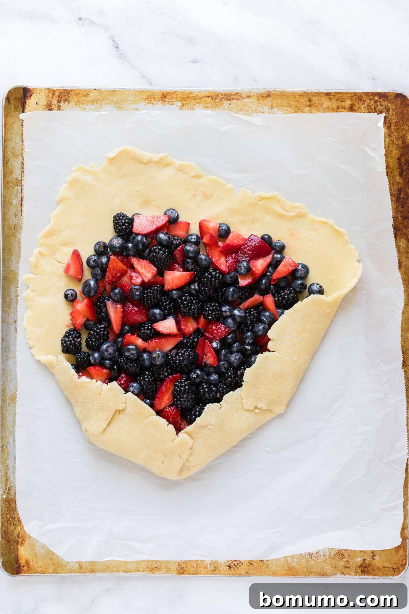 The pie crust is partially folded over the berry filling, showcasing the initial stages of assembly.