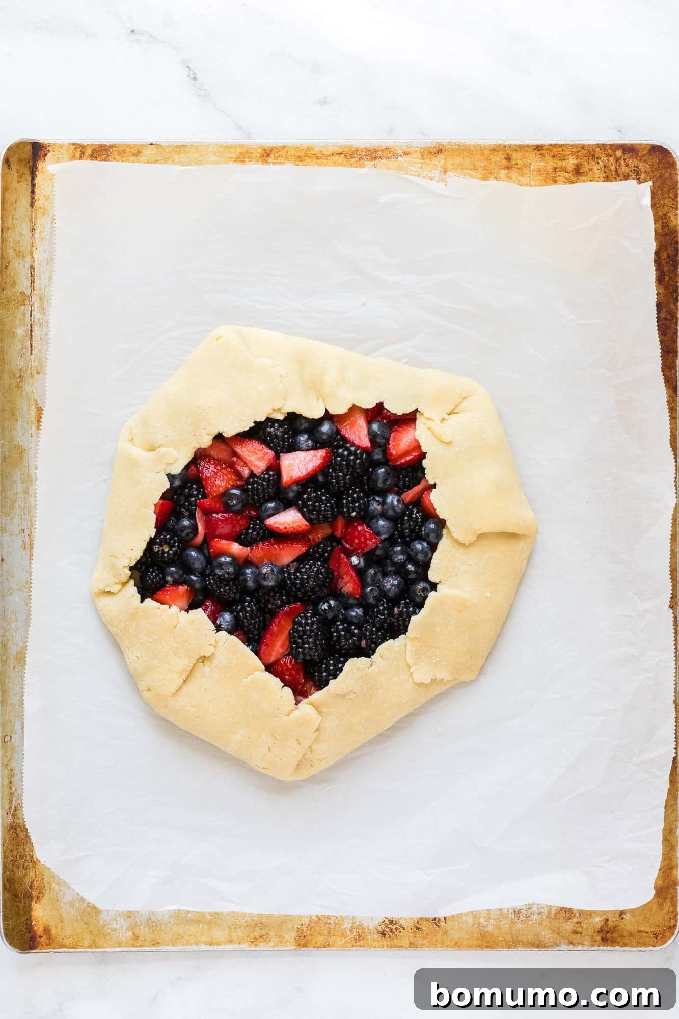 The assembled berry galette, perfectly pleated on a sheet pan, awaiting its turn in the oven.