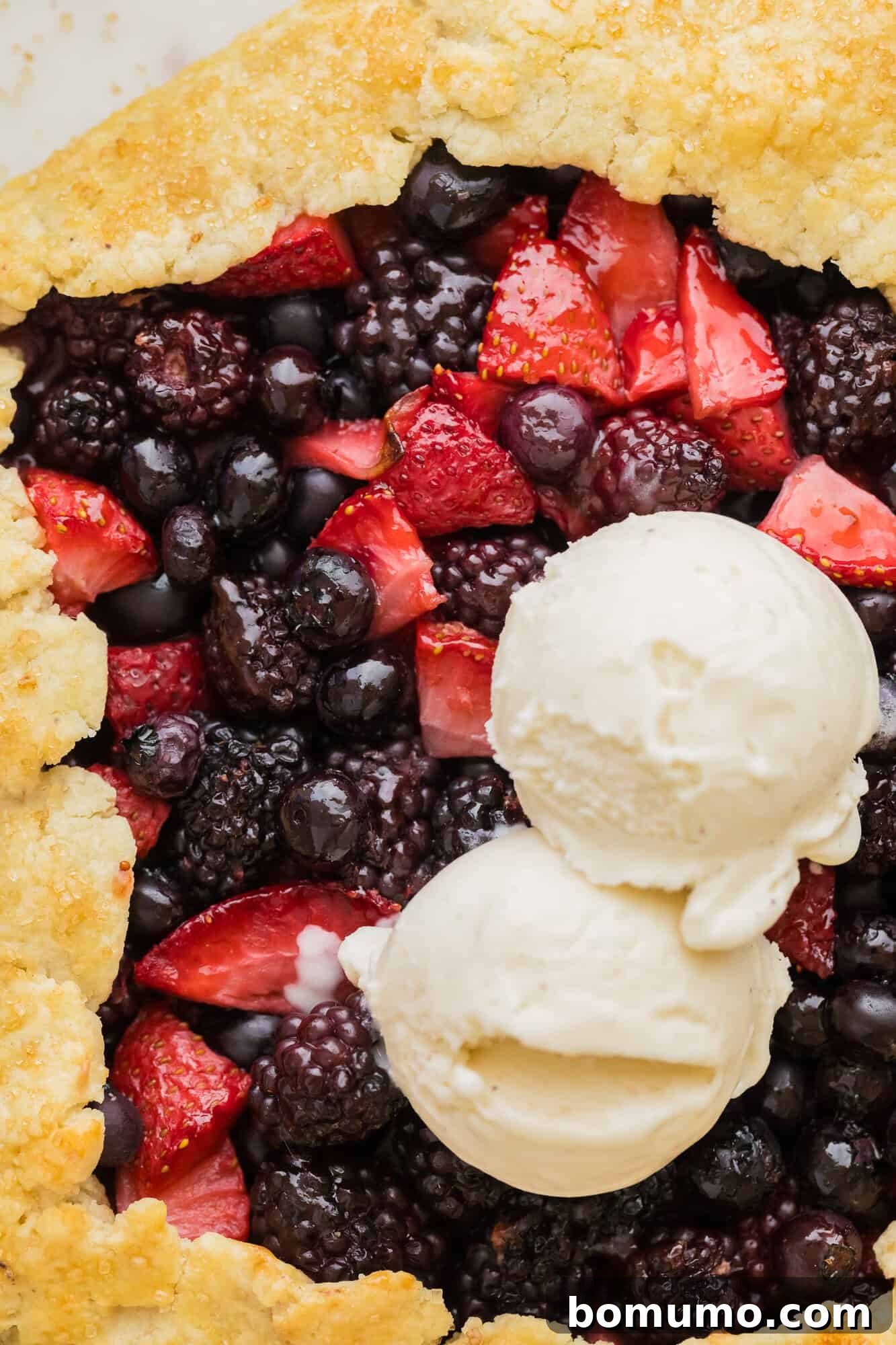 A glorious berry galette, fresh from the oven, adorned with two scoops of creamy vanilla ice cream.