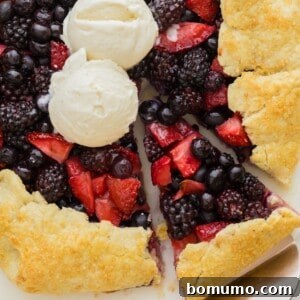 Berry galette, topped with two scoops of vanilla ice cream, one slice cut.