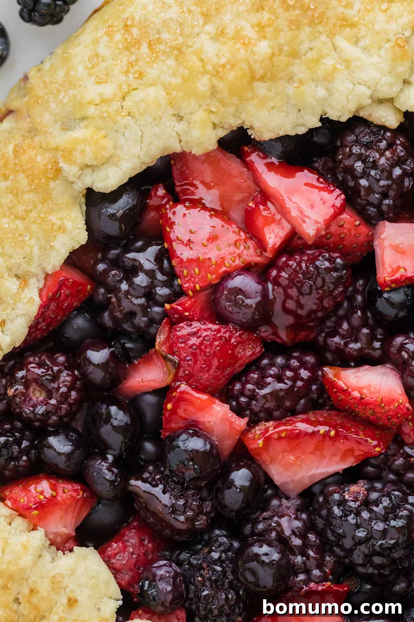 A close-up view of a berry galette, featuring a delightful mix of strawberries, blueberries, and blackberries peeking from under the golden crust.