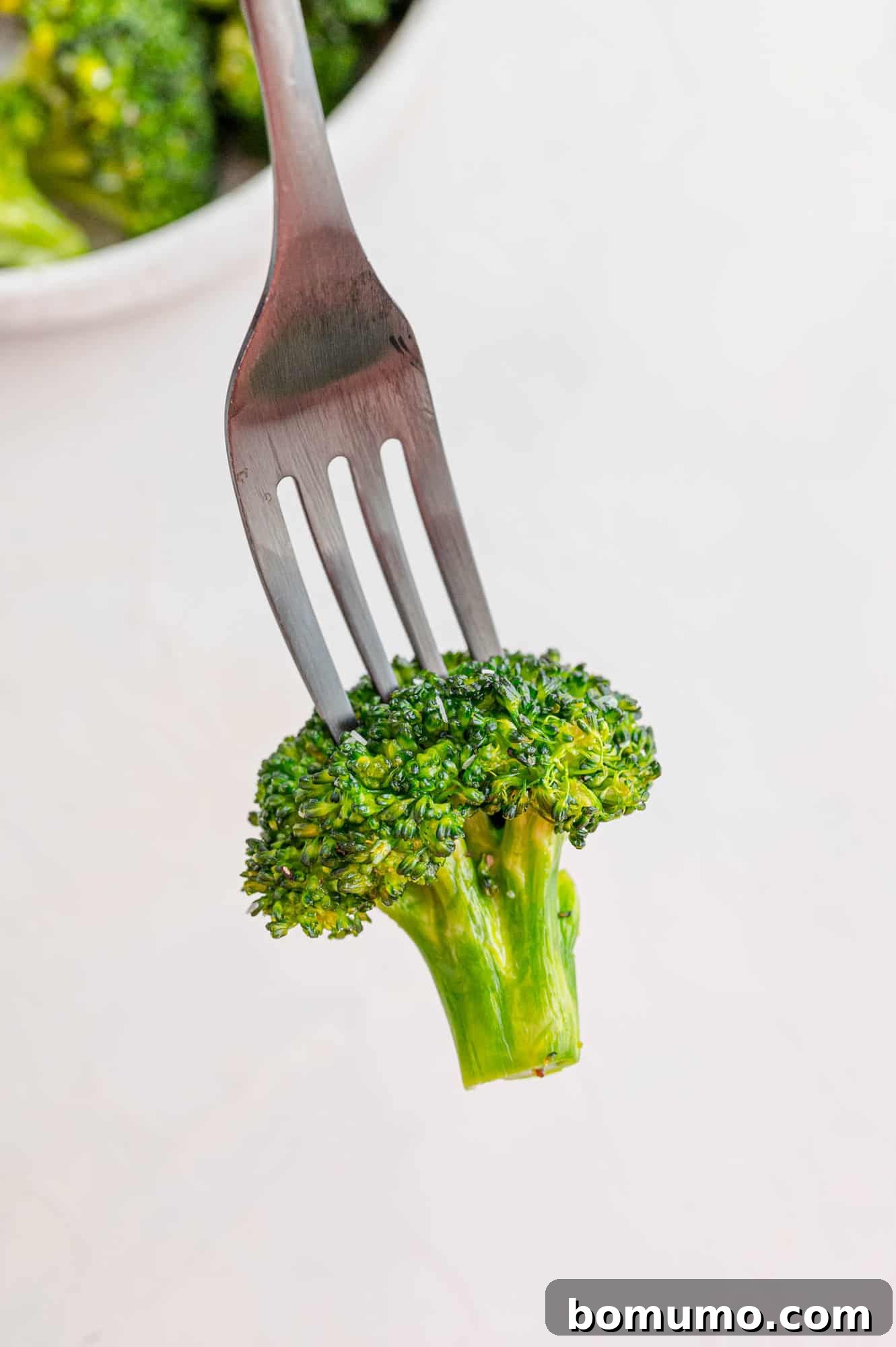 A close-up of a single crispy air fryer broccoli floret perched on the tines of a fork, ready to be eaten.