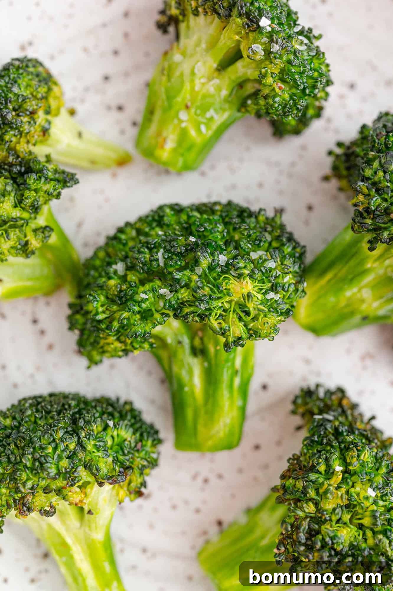 Close-up of perfectly cooked and seasoned broccoli florets on a clean white background, showcasing their tender-crisp texture.
