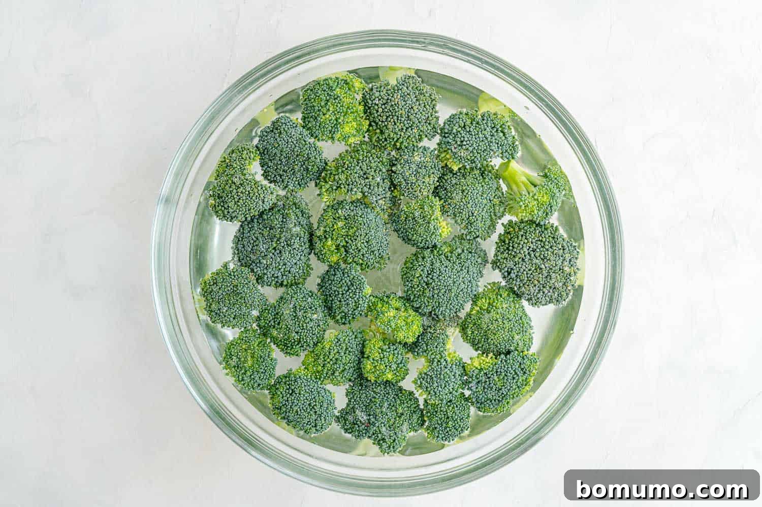 Freshly cut broccoli florets soaking in a clear bowl of water, preparing for air frying.