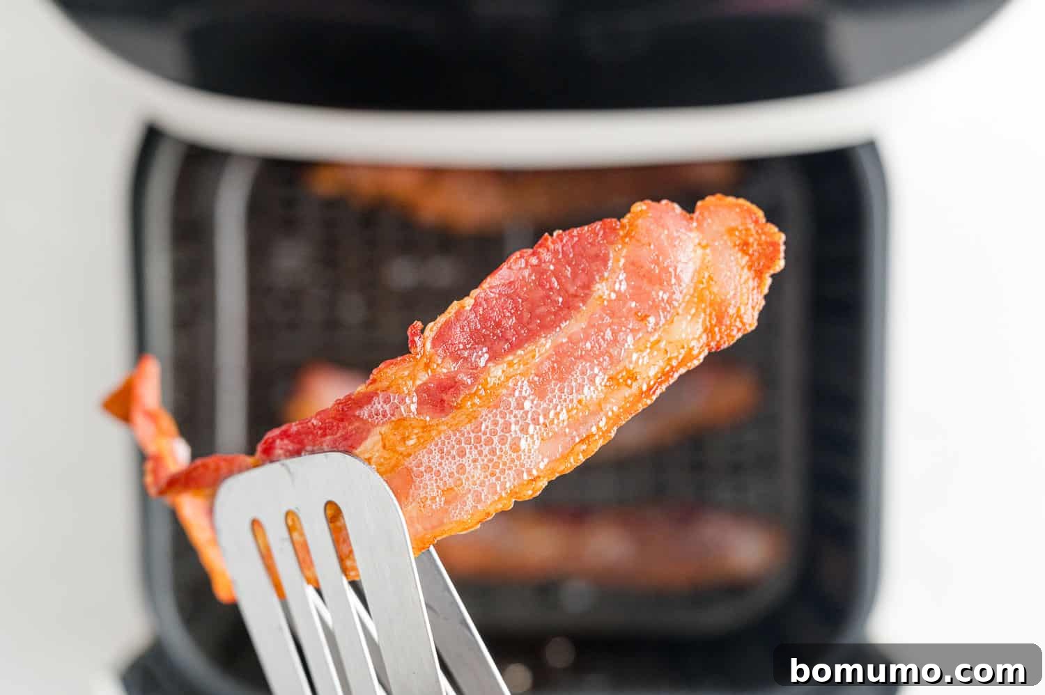 Crispy Air Fried Bacon 8 A perfectly cooked, crispy strip of bacon being held with tongs after being air fried.