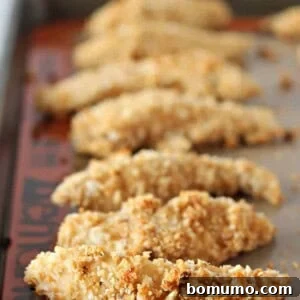 Baked chicken tenders on rimmed baking sheet, golden and crispy.