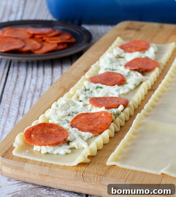 Lasagna noodle with cheese mixture and pepperoni on top of it.