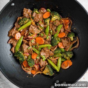 Beef and vegetable stir fry in a black wok.