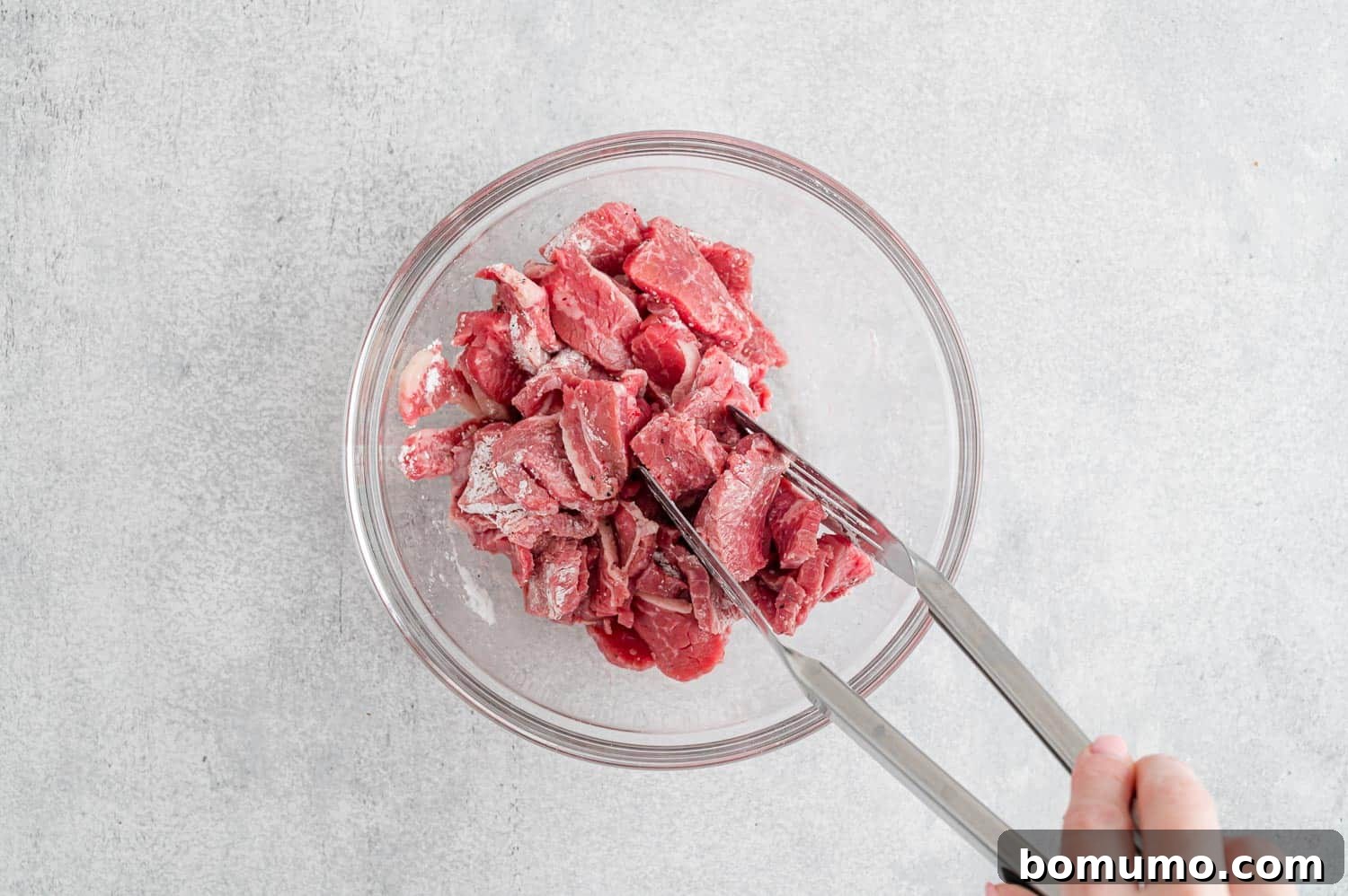 Thinly sliced beef being tossed with a cornstarch mixture in a bowl, preparing it for stir-frying.