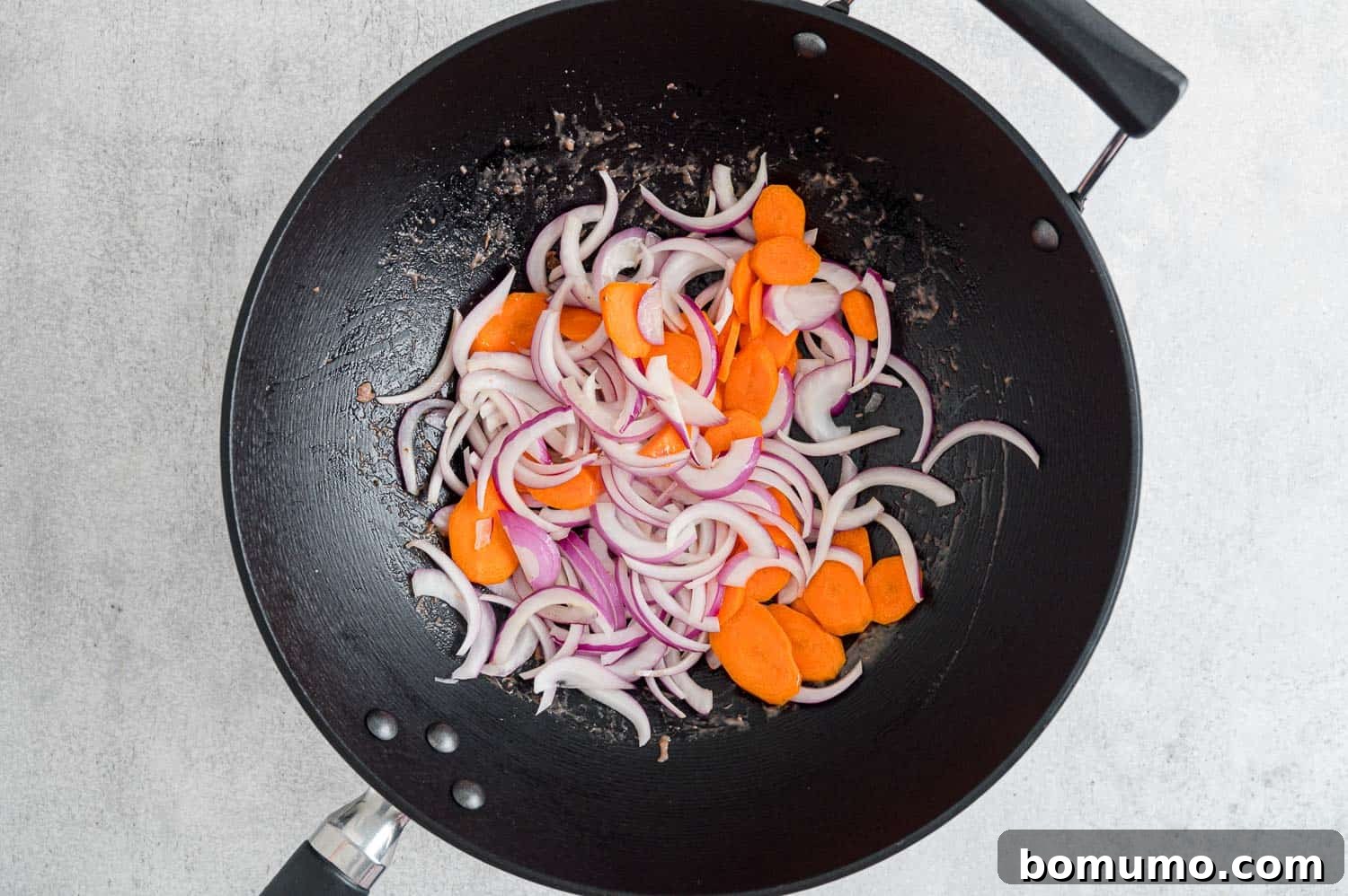 Sliced carrots and onions sizzling in a hot wok, beginning their stir-fry journey.