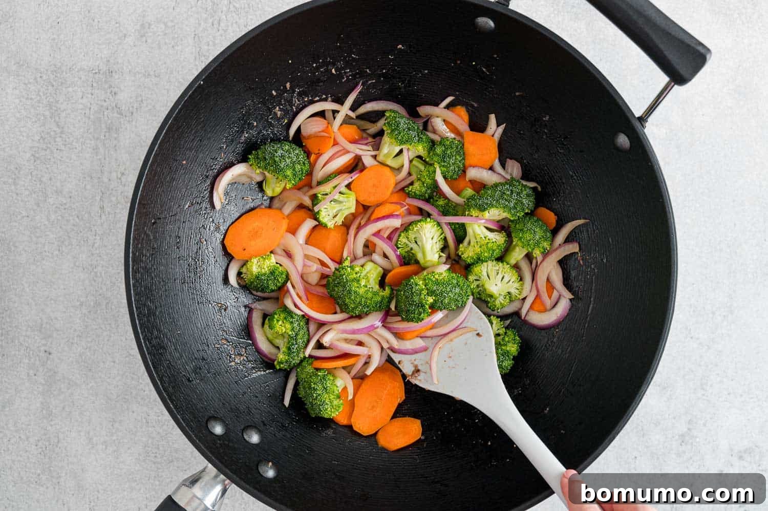 Broccoli florets joining the carrots and onions in the pan, actively stir-frying.