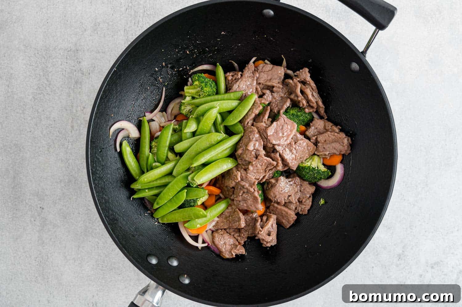 Cooked beef and fresh peas being added to the stir-fry, ready for the sauce.
