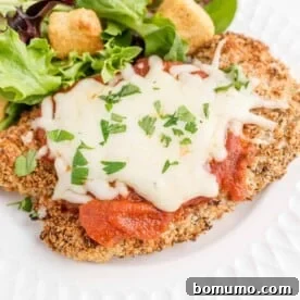 Classic chicken parmesan served on a white plate, beautifully accompanied by a fresh green salad for a perfectly balanced meal.