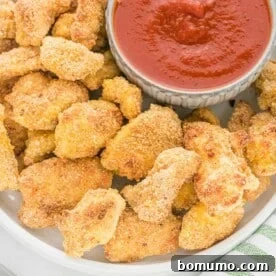 A plate of golden-brown, healthy chicken nuggets with Parmesan, accompanied by a side of classic pizza sauce for dipping.