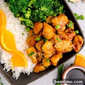 Homemade orange chicken served on a black plate with fresh broccoli and fluffy white rice, creating a colorful and balanced meal.