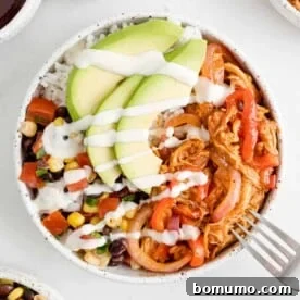 A vibrant BBQ chicken burrito bowl, beautifully topped with creamy avocado slices and a dollop of sour cream.
