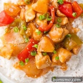 A serving of sweet Hawaiian crockpot chicken, adorned with colorful bell peppers, onions, and juicy pineapple, over rice and garnished with sesame seeds and green onions.