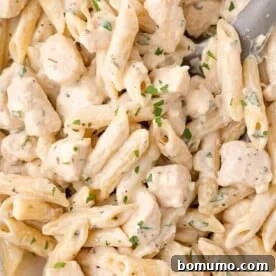 A close-up view of creamy chicken pasta featuring penne, succulent chicken chunks, and a fresh parsley garnish, highlighting its rich texture.