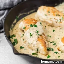 A perfectly cooked chicken breast in a black pan, bathed in a luscious creamy mustard sauce, garnished with fresh herbs.