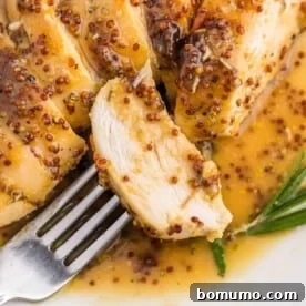 A tender slice of baked chicken on a fork, generously coated in a shimmering honey mustard sauce, ready to be savored.