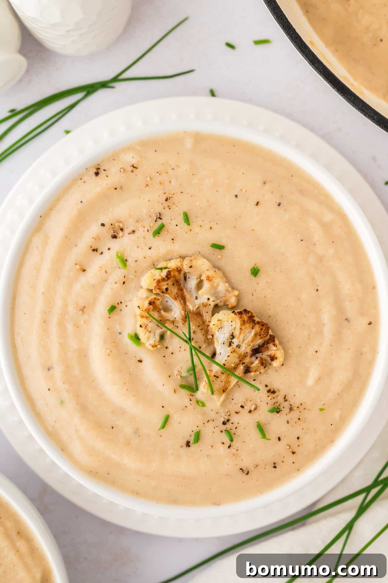 A comforting bowl of roasted cauliflower soup, garnished with extra roasted florets and fresh chives.