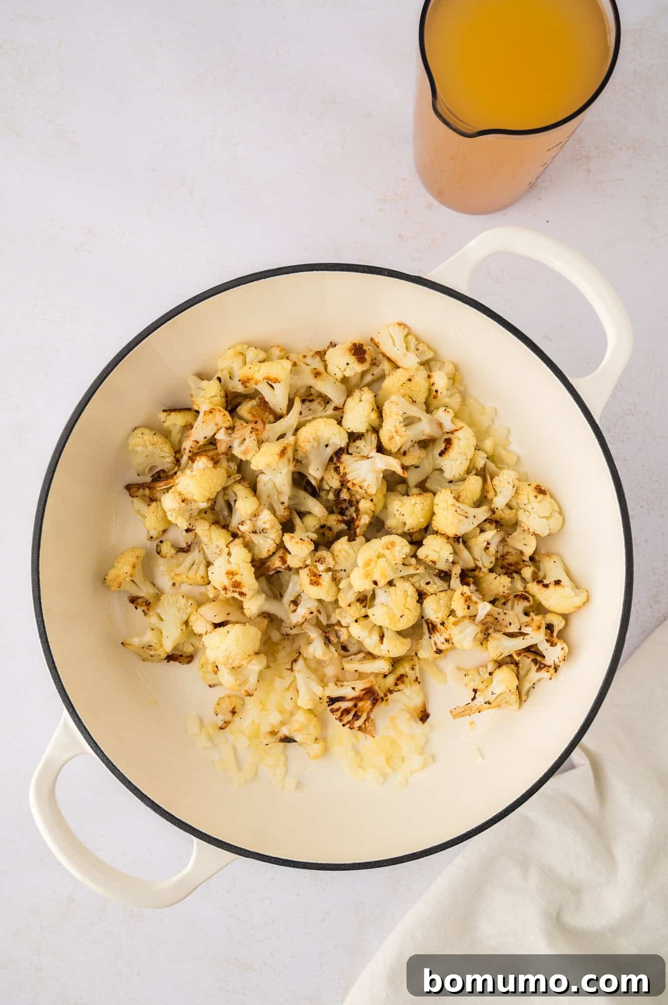 Roasted cauliflower florets being added to the saucepan with sautéed onions and garlic, ready for simmering.