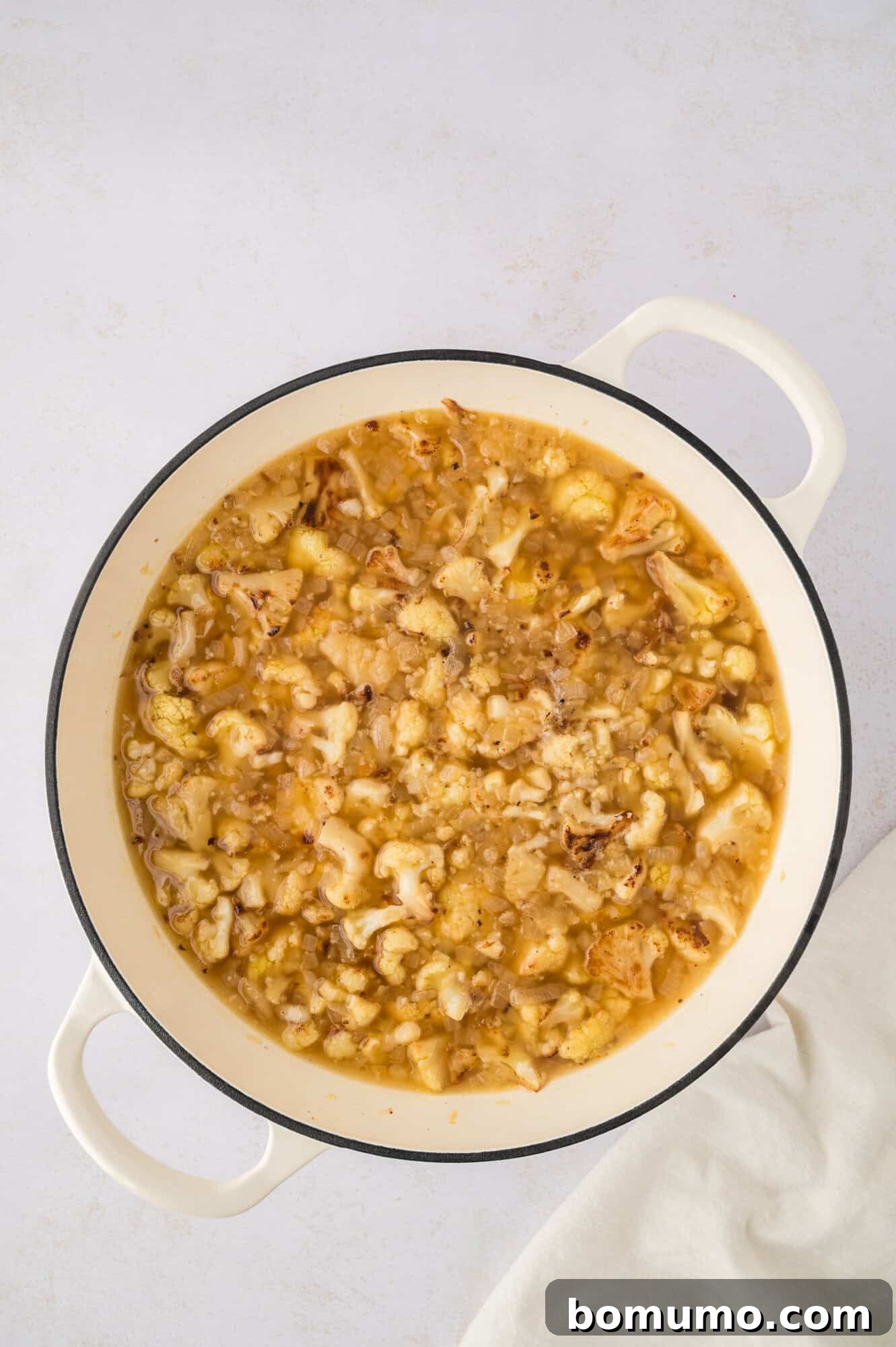 The roasted cauliflower and broth simmering gently in a Dutch oven, the cauliflower becoming tender and flavors deepening.