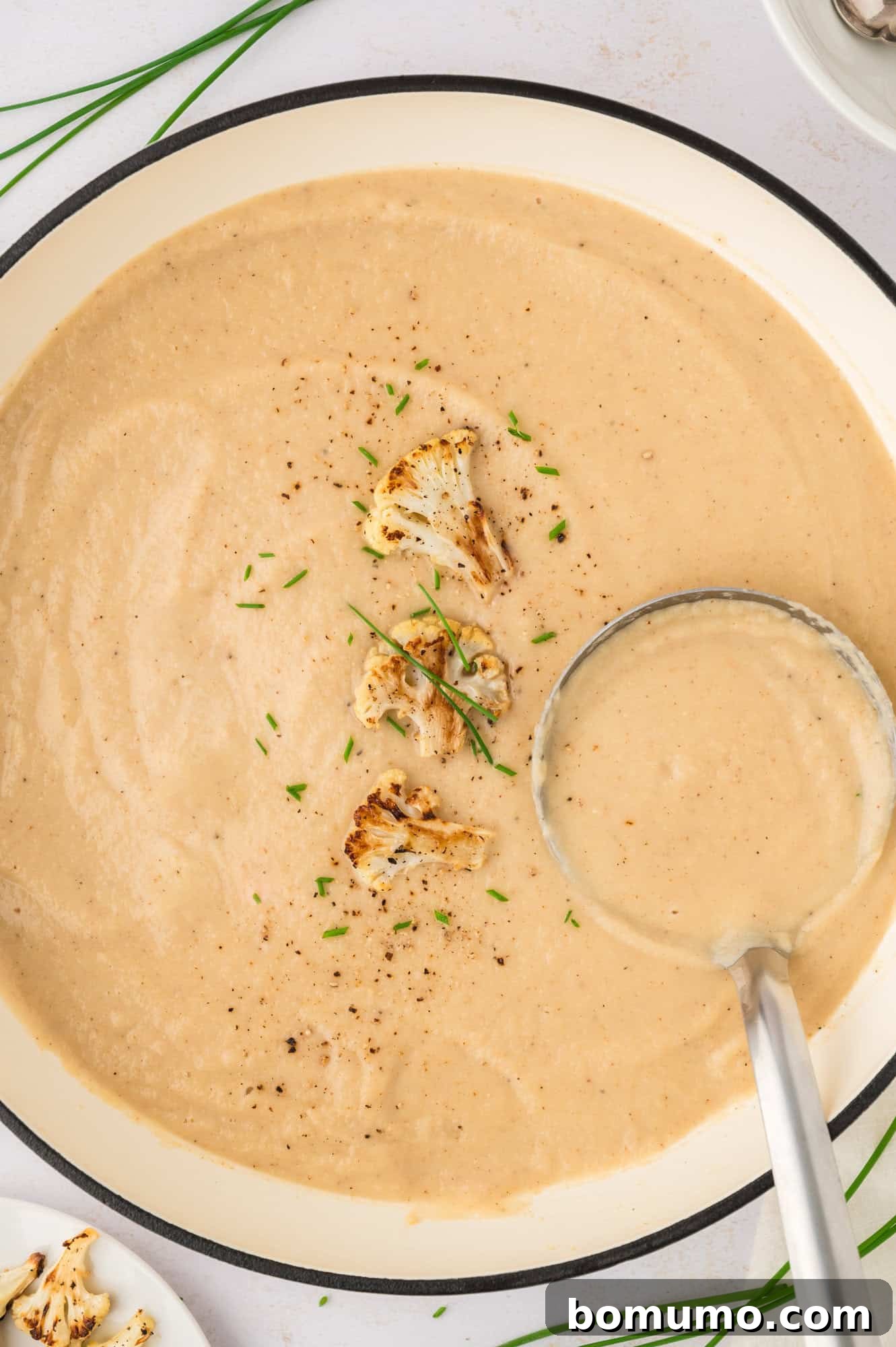 A large pot of creamy roasted cauliflower soup, ready to be served, with a ladle resting inside.