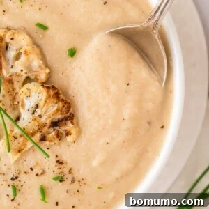 A bowl of roasted cauliflower soup, perfectly creamy and garnished with chives and roasted cauliflower florets.