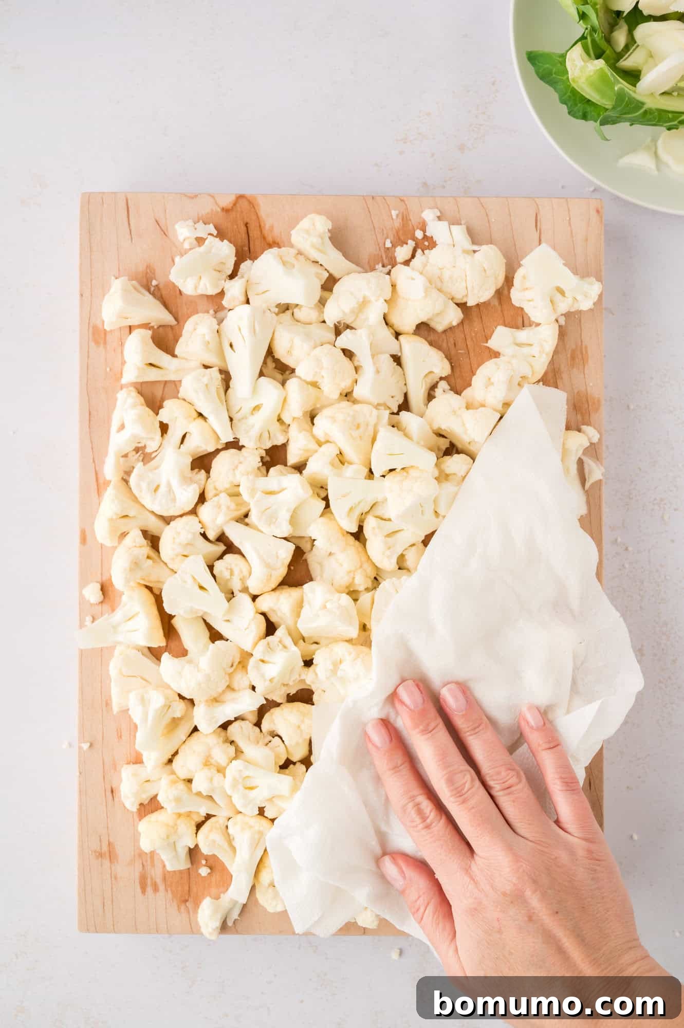 Freshly cut cauliflower florets being patted dry with a clean kitchen towel, a crucial step before roasting for optimal browning.