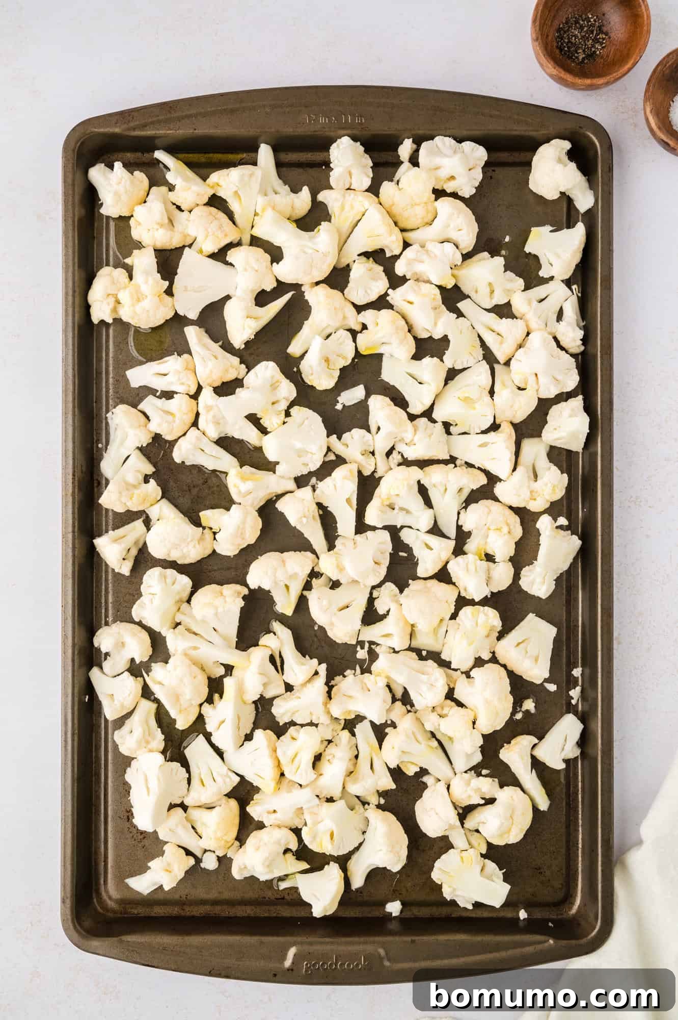 Raw cauliflower florets arranged in a single layer on a baking sheet, seasoned and ready for roasting.