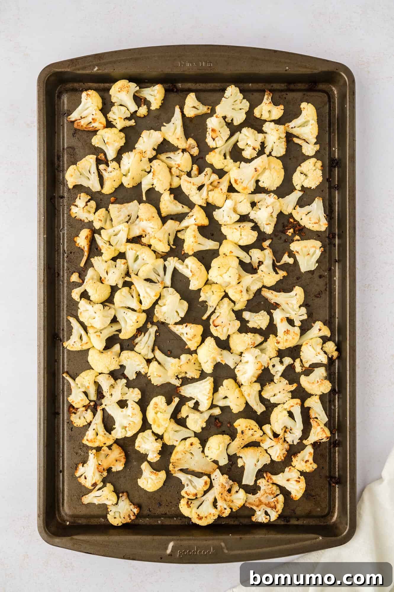 Golden-brown and tender roasted cauliflower florets spread across a baking sheet, showcasing the perfect caramelization achieved in the oven.