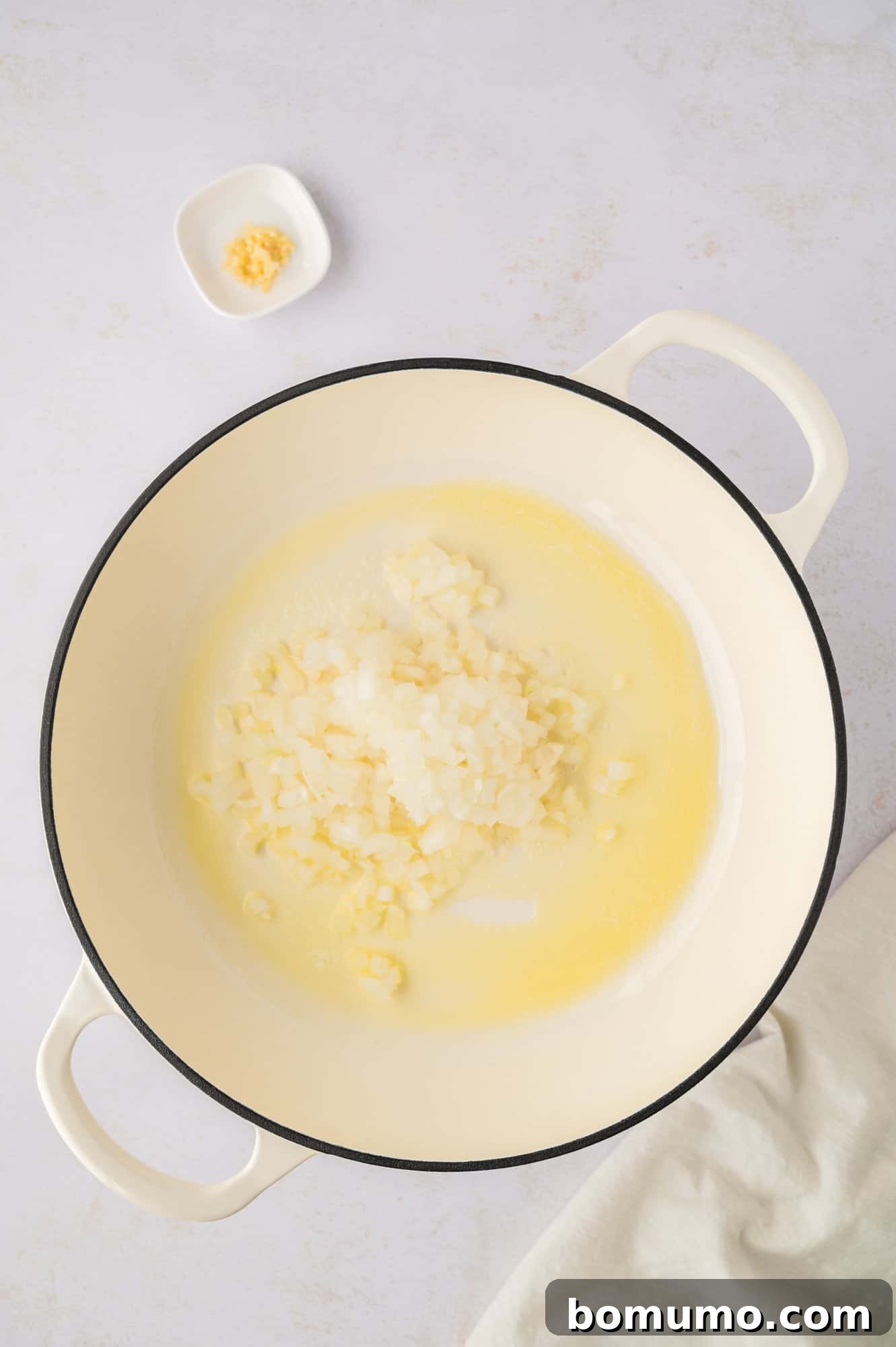 Diced yellow onions being added to melted butter in a pan, ready to be sautéed until translucent and sweet.