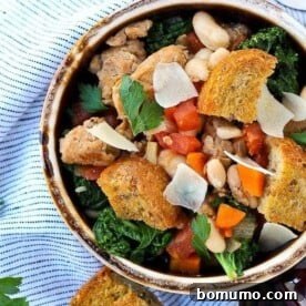 Overhead view of an earthenware bowl filled with Italian sausage, white bean, and kale stew, garnished with large croutons.