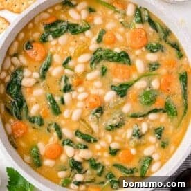 A pot of hearty white bean soup, richly flavored with spinach, carrots, and a creamy broth, ready to serve.