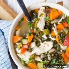 Colorful bowl of soup with chicken, kale, carrots, and cannellini beans.