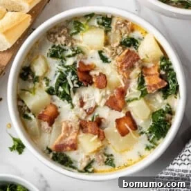 Overhead view of Zuppa Toscana soup in a white bowl, elegantly garnished with crispy bacon.