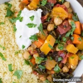 Close up overhead view of vibrant Moroccan stew made with butternut squash, chickpeas, and more, served alongside couscous.