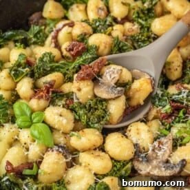 Close-up view of one pan gnocchi on a serving spoon, with sun-dried tomatoes and kale clearly visible.