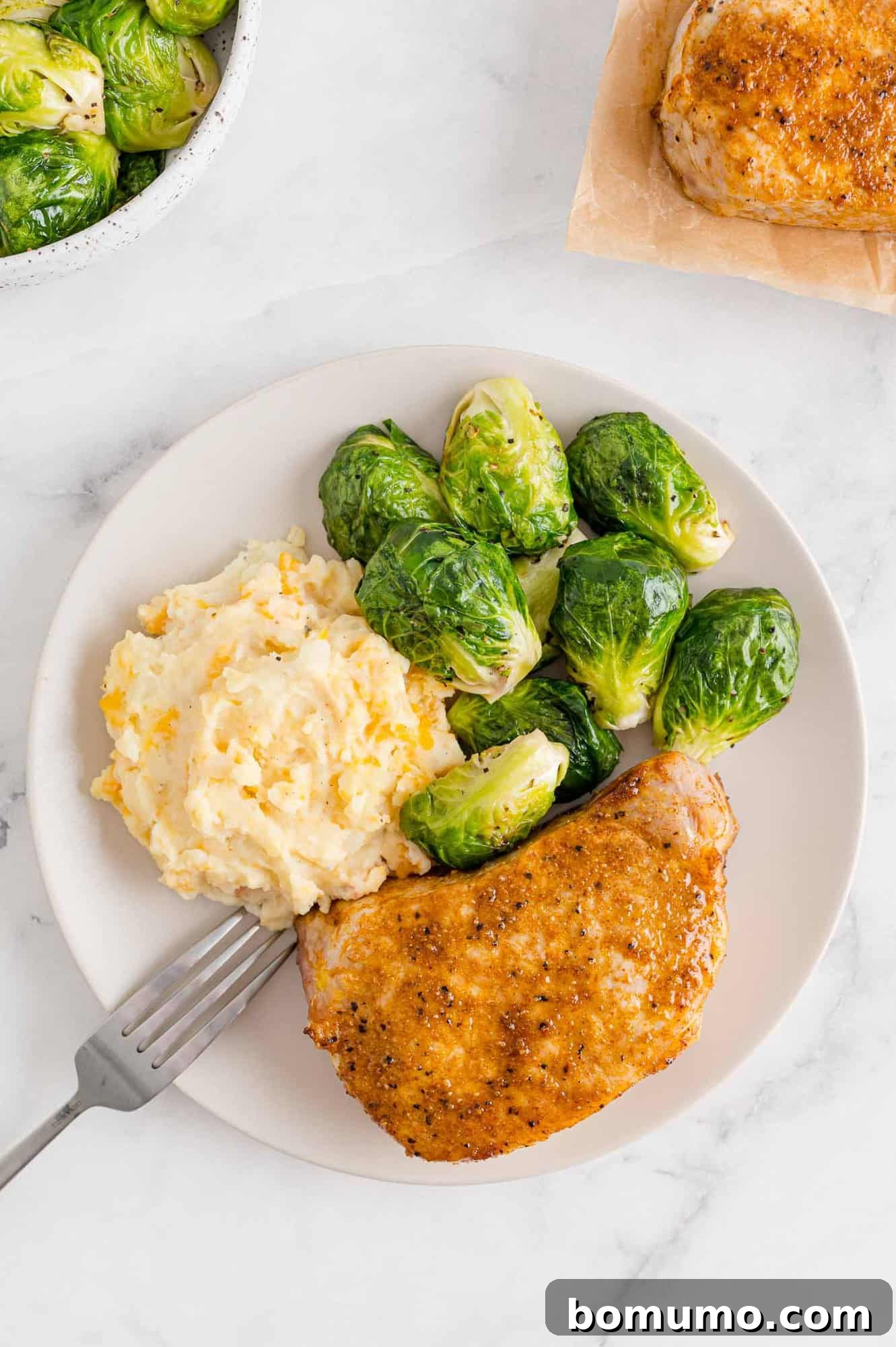 Air fryer pork chops served on a plate with roasted potatoes and Brussels sprouts.