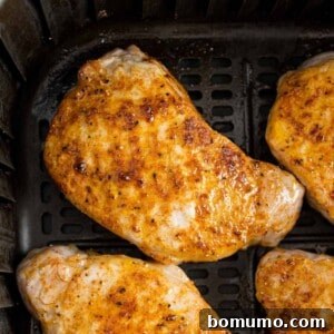 Air fryer pork chops in the basket of an air fryer, golden brown and perfectly cooked.