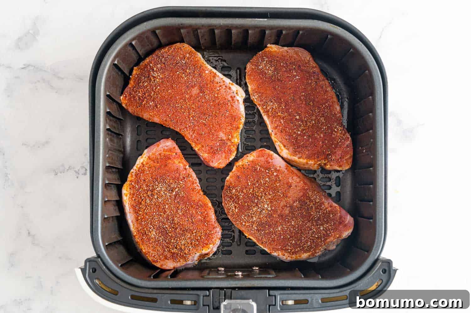 Uncooked seasoned pork chops arranged in an air fryer basket.