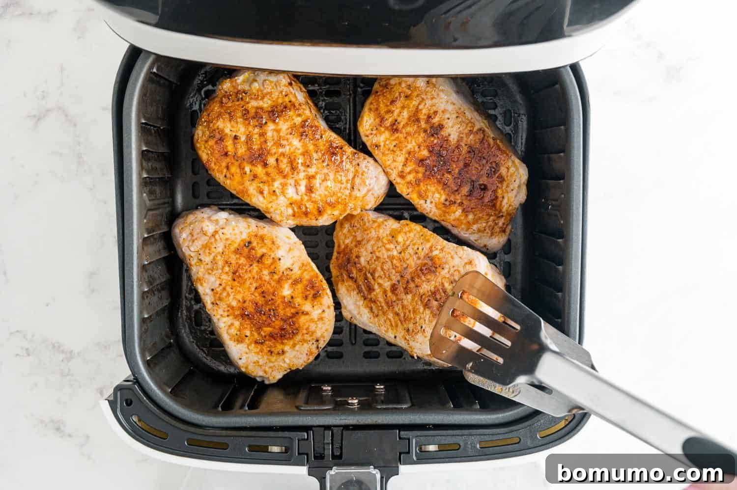 A seasoned pork chop being flipped in an air fryer basket.