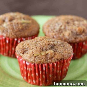 Three apple bran muffins with red liners on a green plastic plate.